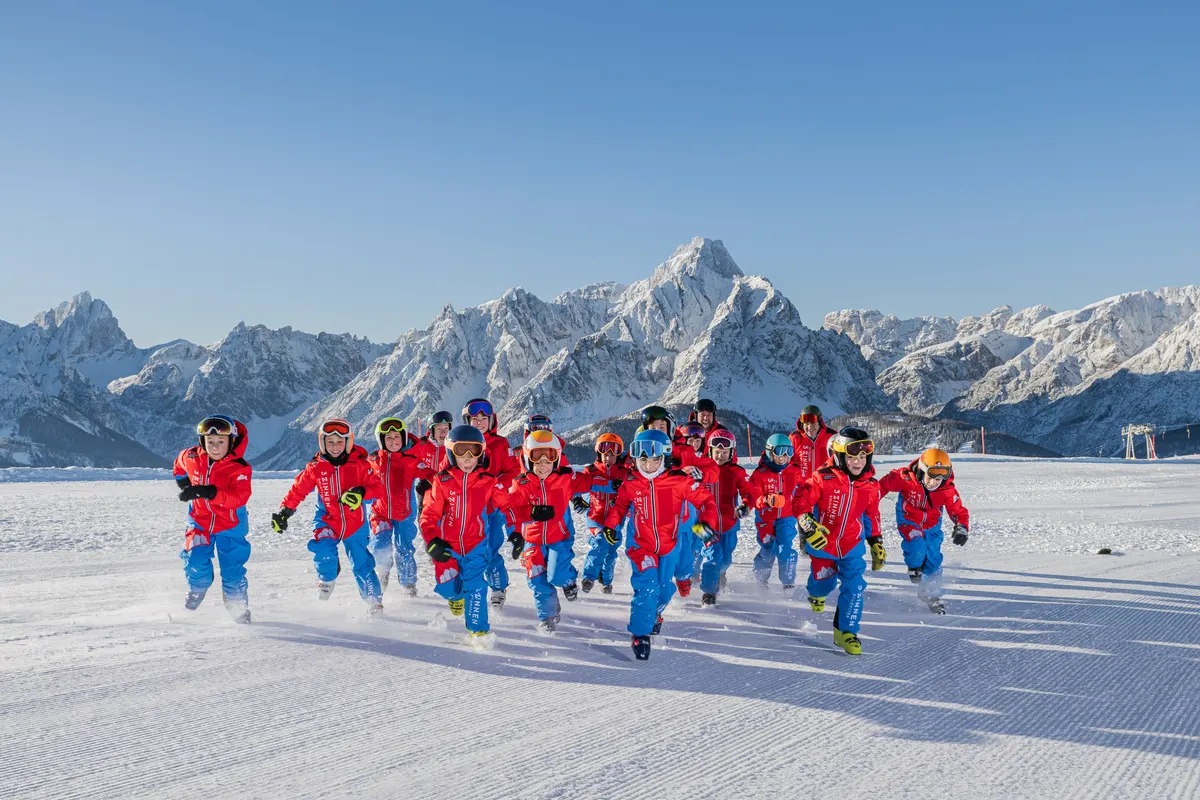 Kindergruppe in roten Clubjacken und blauen Skihosen läuft über die Piste